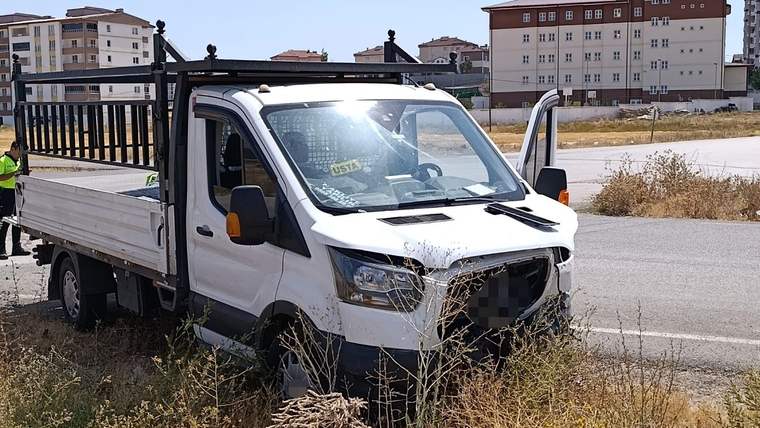 Ön kısmı hasar görmüş beyaz kasalı kamyonet, yol kenarındaki kuru otların arasında duruyor.