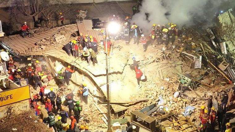 Gece çöken binanın enkazında, yoğun duman arasında çok sayıda kurtarma görevlisi ve insan görülüyor.
