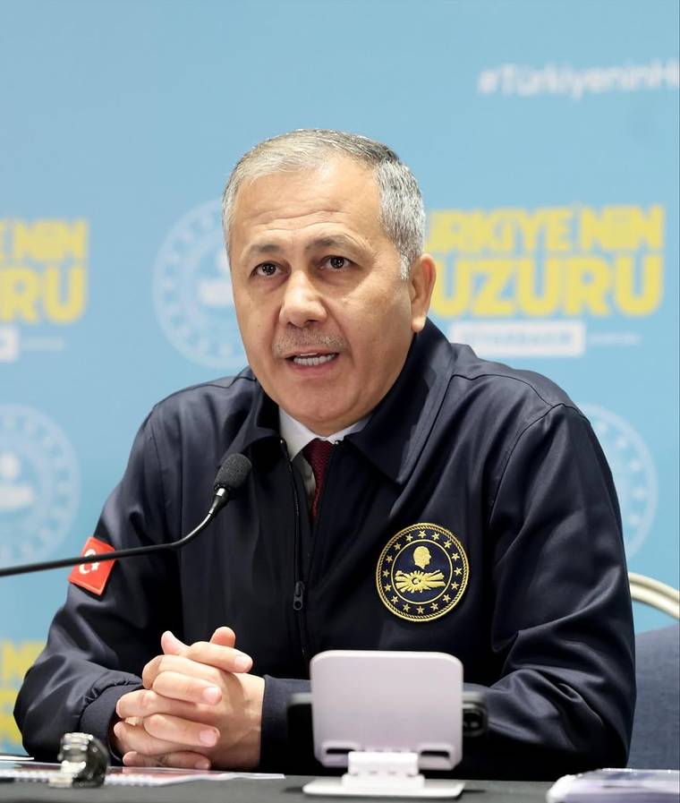 Mikrofon önünde konuşan, göğsünde yıldızlı arma bulunan koyu renkli üniformalı bir kişi görülüyor.