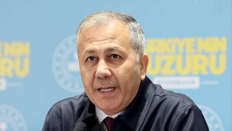 Mikrofon önünde konuşan, göğsünde yıldızlı arma bulunan koyu renkli üniformalı bir kişi görülüyor.