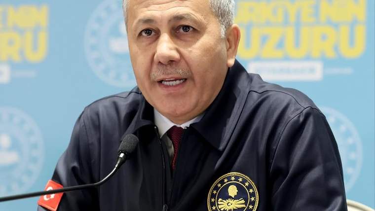 Mikrofon önünde konuşan, göğsünde yıldızlı arma bulunan koyu renkli üniformalı bir kişi görülüyor.