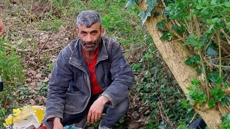 Bir kişi, ağaçların arasında oturarak Kur'an-ı Kerimleri düzenli bir şekilde yerleştiriyor.