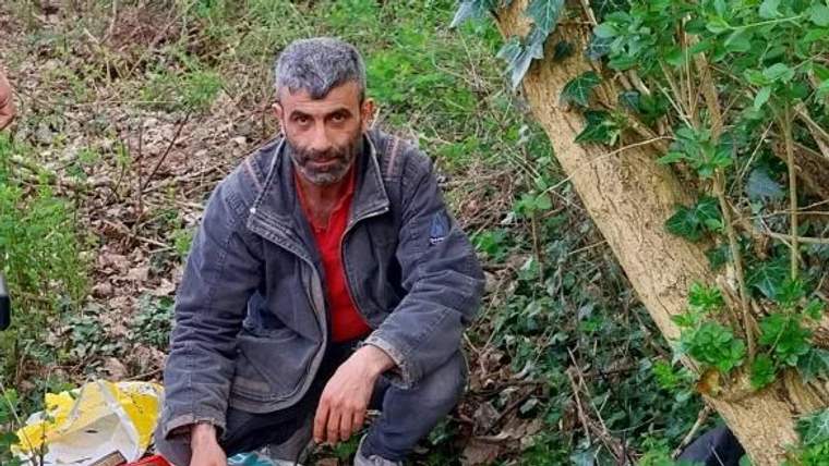 Bir kişi, ağaçların arasında oturarak Kur'an-ı Kerimleri düzenli bir şekilde yerleştiriyor.