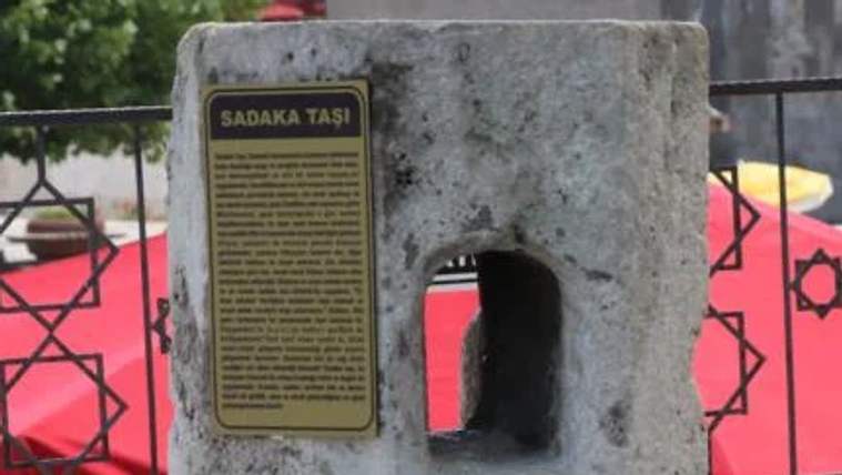 Sadaka taşı, üzerinde açıklama yazılı bir tabela ile birlikte taşın üstünde duruyor.