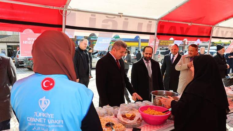 Kırmızı çadır altındaki tezgahta yiyecekler sergilenirken, birkaç kişi stant önünde duruyor.