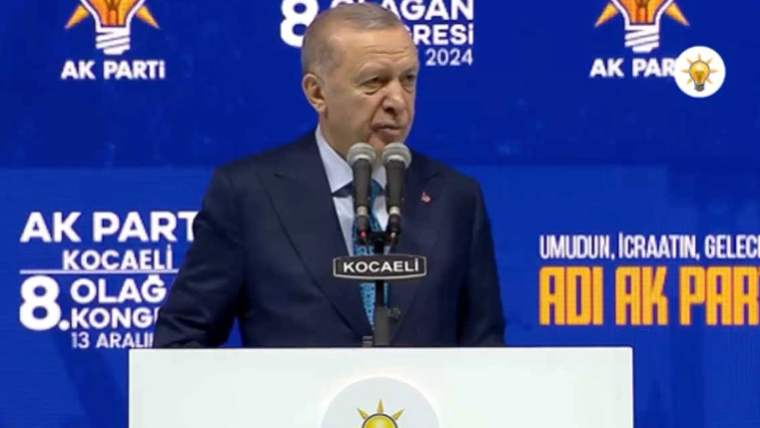Mikrofonun önünde konuşan bir kişi, arka planda AK Parti logosu ve Kocaeli yazısı görünmekte.