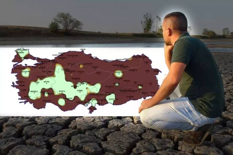 Kurumuş ve çatlamış zeminde oturan bir kişi, renkli Türkiye haritasının bulunduğu panoya bakıyor.