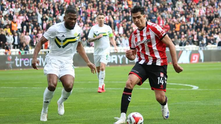 Futbol maçında, Sivasspor'un oyuncusu topu sürerken, rakip oyuncu ona müdahale ediyor.