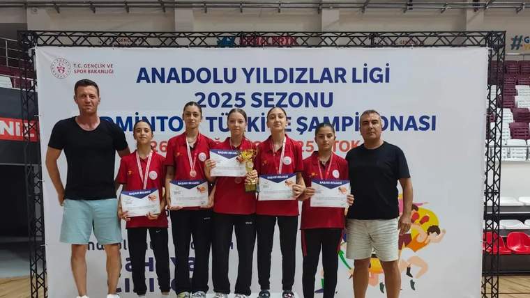 Spor salonunda dört genç sporcu, madalyaları ve belgeleriyle iki yetişkinin yanında podyumda duruyor.