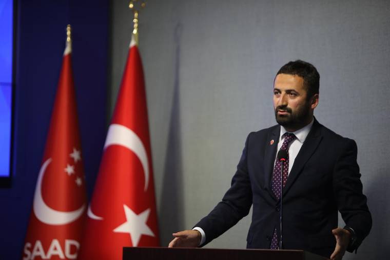 Saadet Partisi'nin logosunun bulunduğu arka planda, bir kişi kürsüde konuşuyor.