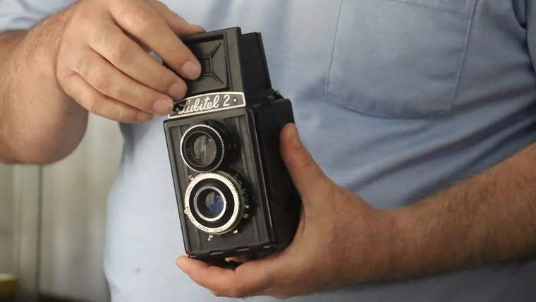 Bir kişi, üzerinde Rolleiflex yazısı bulunan çift objektifli eski bir fotoğraf makinesini ellerinde tutuyor.