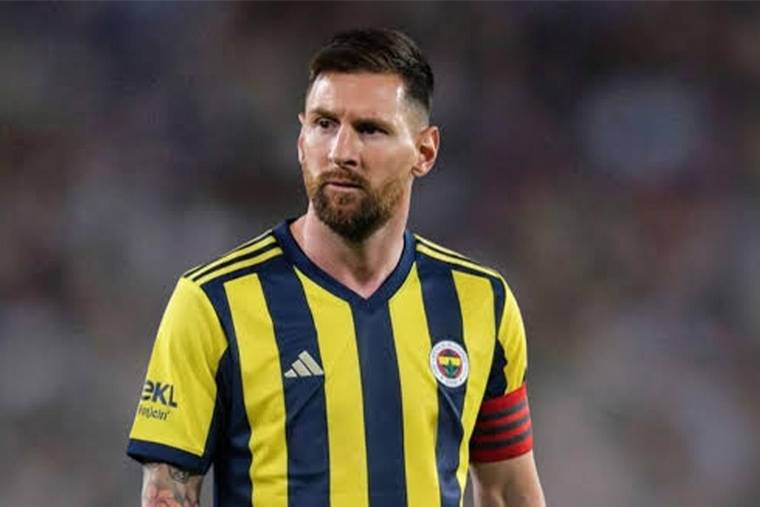 Sarı-lacivert çubuklu forma ve kaptanlık pazubandı takan sakallı bir futbolcu sahada duruyor.