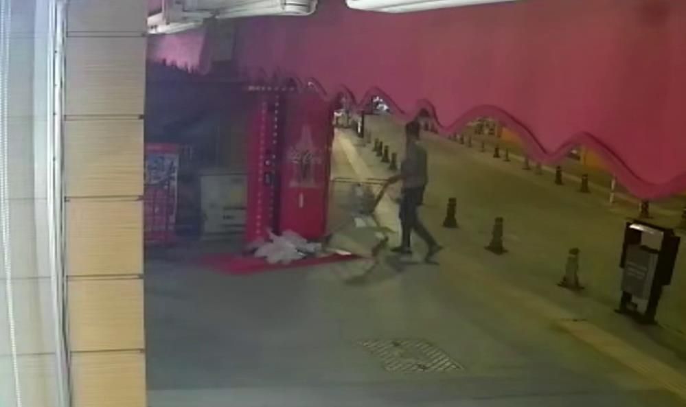 Gece çekiminde bir kişi, market arabasıyla kaldırım boyunca ilerlerken görülüyor.