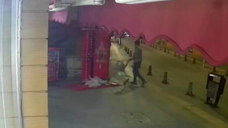 Gece çekiminde bir kişi, market arabasıyla kaldırım boyunca ilerlerken görülüyor.