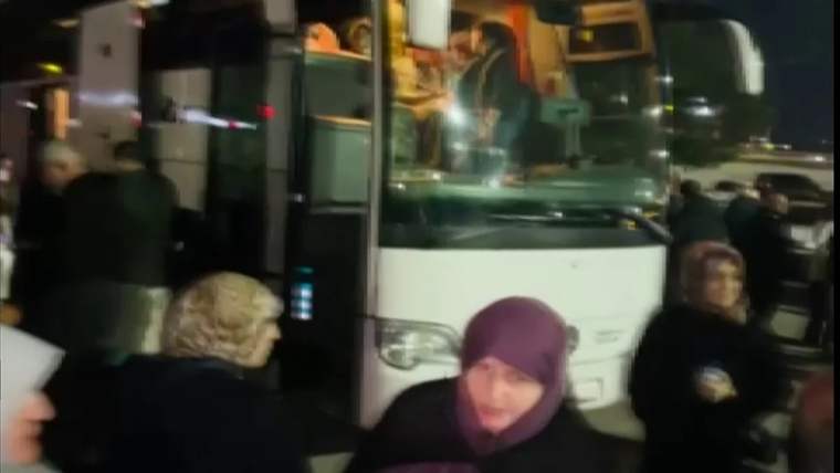 Bir grup insan, otobüsün önünde bekliyor; otobüsün içinde birkaç kişi görünüyor.