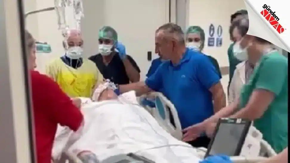 Hastane odasında maskeli sağlık çalışanları, beyaz örtülü bir hastanın bulunduğu yatağın çevresinde duruyor.