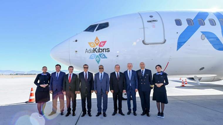 Üzerinde “Ada Kıbrıs” yazan yolcu uçağının önünde, üniformalı ve takım elbiseli dokuz kişi duruyor.