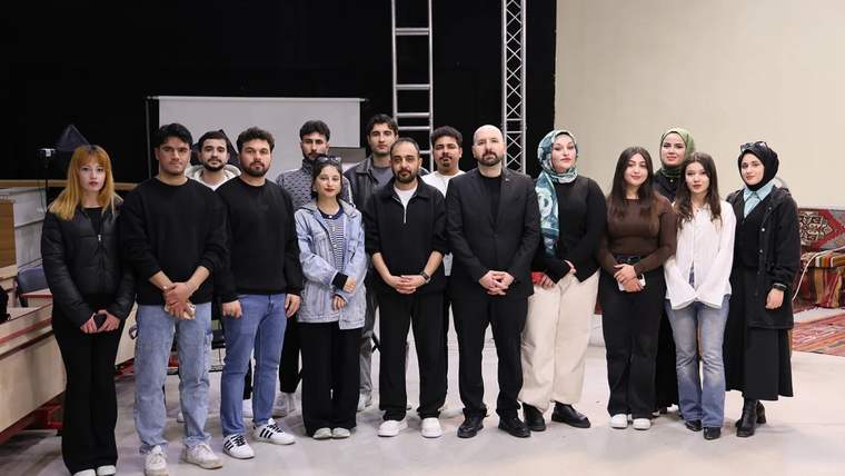 Bir grup insan, stüdyoda poz veriyor; bazıları siyah, bazıları beyaz kıyafetler giymekte.