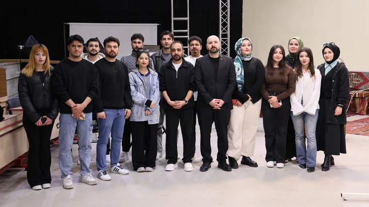 Bir grup insan, stüdyoda poz veriyor; bazıları siyah, bazıları beyaz kıyafetler giymekte.