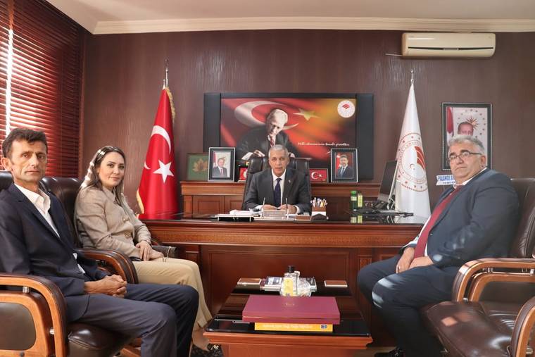 Bir masa etrafında oturan dört kişi, arka planda Türk bayrağı ve Atatürk posteri var.
