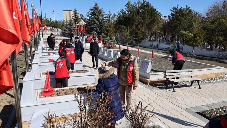 Şehitlikte, Türk bayraklarıyla çevrili mezarların bakımını yapan kişiler, mezarları düzenliyor.