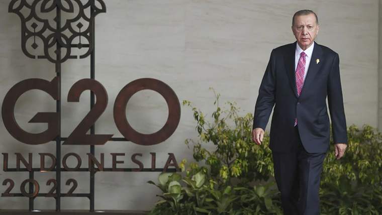 G20 logosunun önünde yürüyen bir kişi, resmi bir kıyafet giymekte.