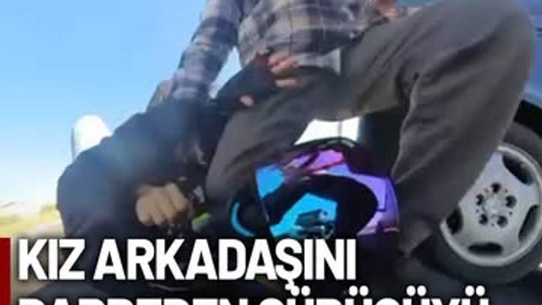 Ekose gömlekli bir kişi, otomobilin yanında yerde bulunan başka bir kişinin üzerinde duruyor.