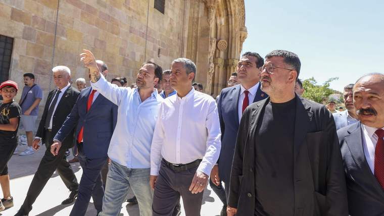 Bir grup insan, tarihi bir binanın önünde yürüyerek sohbet ediyor. Bazıları resmi kıyafetler giymekte.