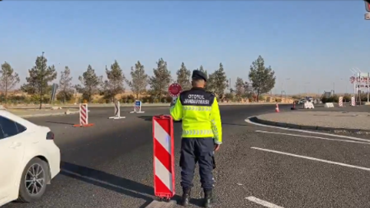 Yolda trafik kontrolü yapan bir polis memuru, elinde dur işareti tutuyor.
