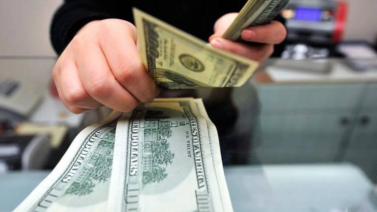Bir kişinin elleri, banknot sayma makinesi önünde ABD doları banknotlarını sayarken görülüyor.