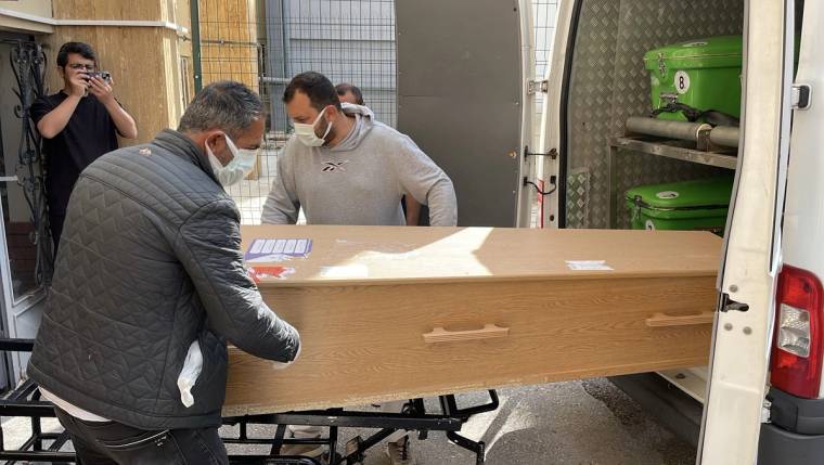 İki kişi, bir cenazeyi beyaz bir araca yerleştiriyor.