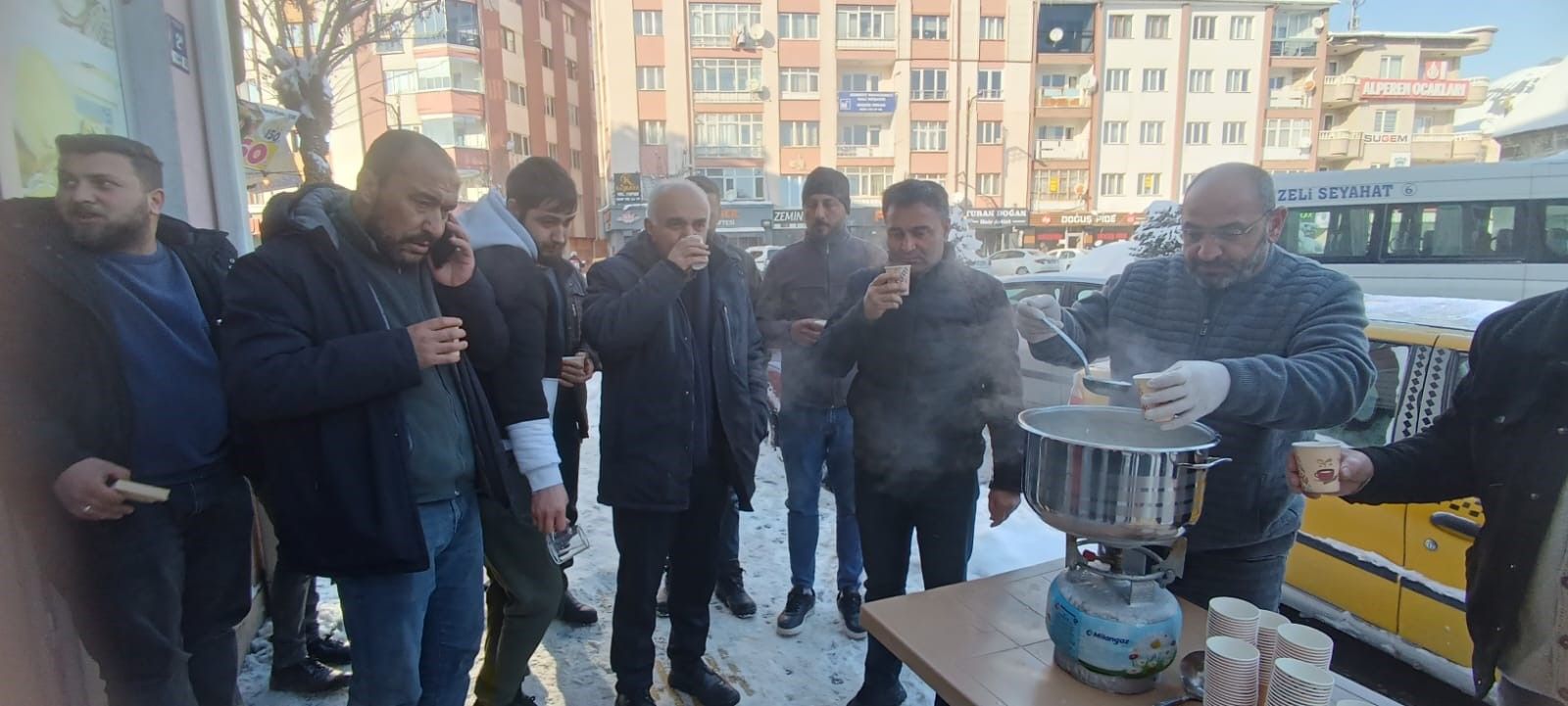 Karla mücadele eden belediye işçileri, sıcak süt içen kalabalık bir grup etrafında toplanmış.