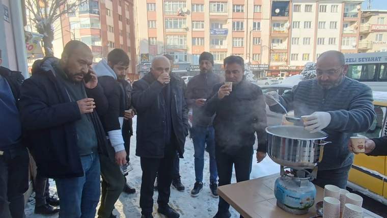 Karla mücadele eden belediye işçileri, sıcak süt içen kalabalık bir grup etrafında toplanmış.