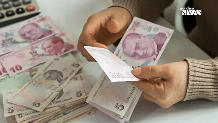 Bir kişinin elinde 200 TL banknot tutarken, masada çeşitli banknotlar yer alıyor.