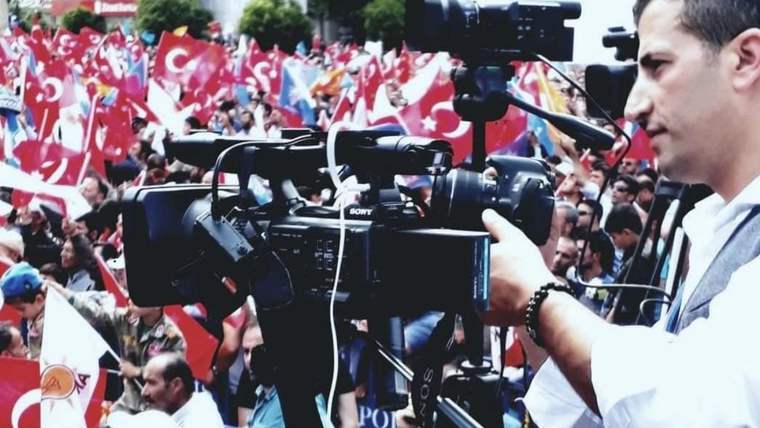 Bir kameraman, kalabalık ve Türk bayrakları önünde birden fazla profesyonel video kamerasını kullanıyor.
