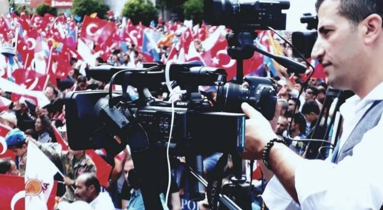 Bir kişinin kullandığı televizyon kameralarının önünde Türk bayrakları taşıyan kalabalık görülüyor.