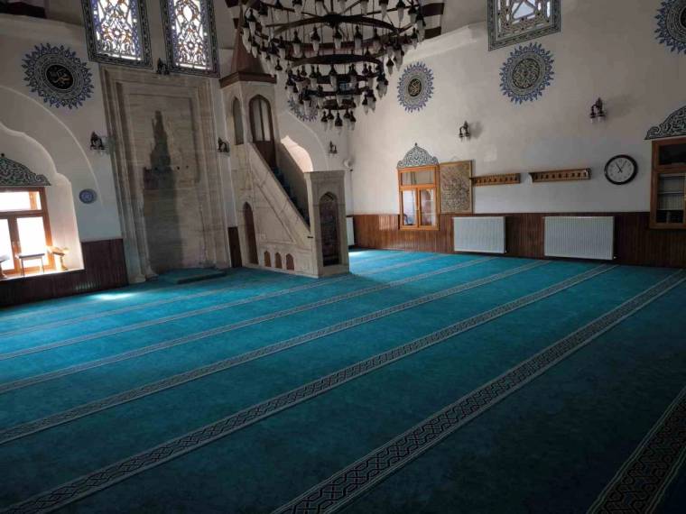 İç mekânda mihrap, minber, süslemeli pencereler ve turkuaz halılarla kaplı geniş bir cami alanı