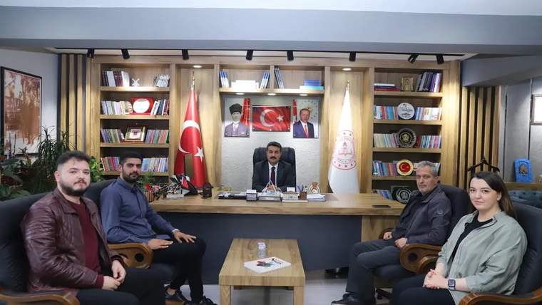 Makam odasında bir masa çevresinde oturan beş kişi, Türk bayrağı ve kitaplıkların önünde görülüyor.
