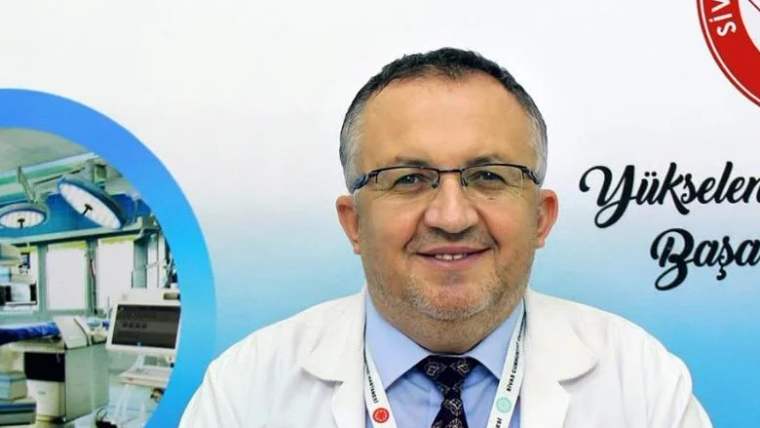 Beyaz önlük giymiş bir doktor, gülümseyerek kameraya bakıyor.