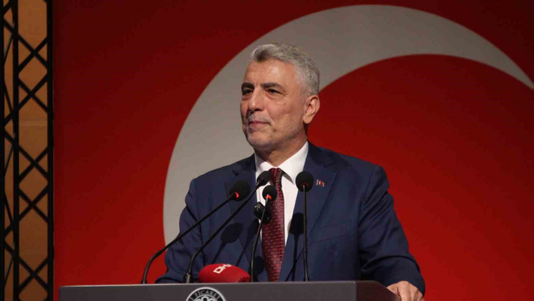Kürsüde konuşan gri saçlı bir kişi, arkasında ay yıldızlı kırmızı fon ve mikrofonlarla görülüyor.