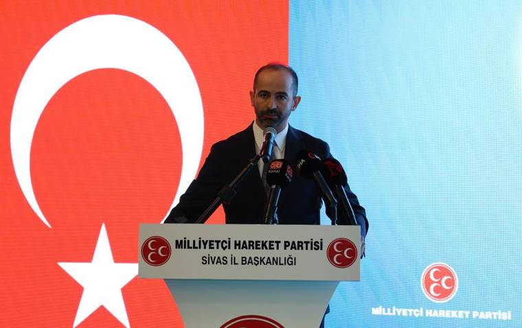 Kürsüde konuşan bir kişi, üzerinde Milliyetçi Hareket Partisi Sivas İl Başkanlığı yazan pankartın önünde duruyor.