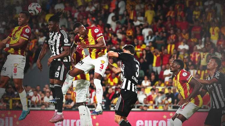 Futbol maçında siyah-beyaz ve sarı-kırmızı formalar giyen oyuncular topa yükselirken mücadele ediyor.