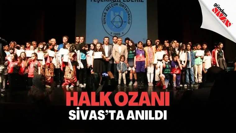 Sahnede çok sayıda öğrenci ve yetişkin, ellerinde belgelerle “Sivas Selçuk Ortaokulu” pankartının önünde duruyor.