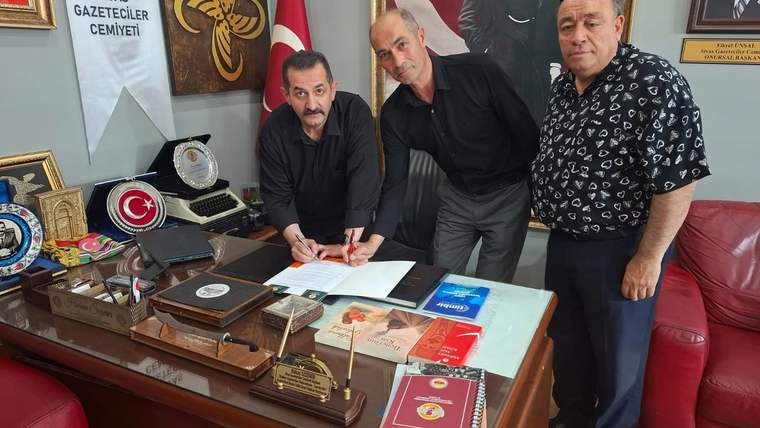 Masada belge imzalayan üç erkek, arkalarında Türk bayrağı ve “Sivas Gazeteciler Cemiyeti” yazılı pankart bulunuyor.