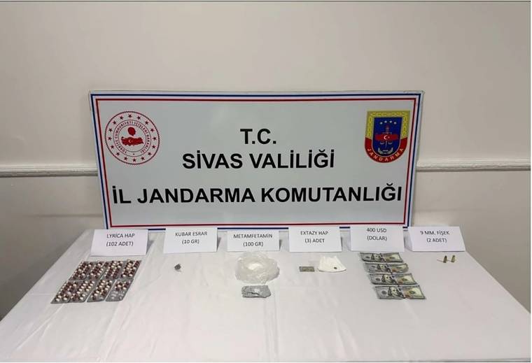 Bir masanın üzerinde çeşitli uyuşturucu maddeler ve sahte dolarlar sergileniyor.