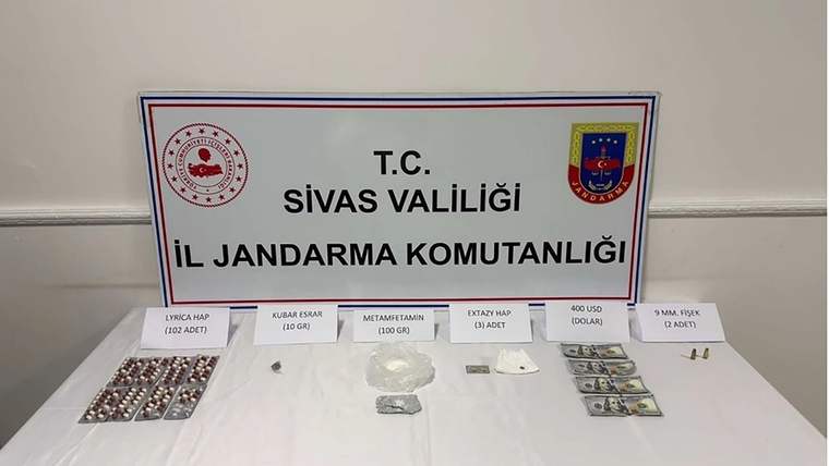 Bir masanın üzerinde çeşitli uyuşturucu maddeler ve sahte dolarlar sergileniyor.