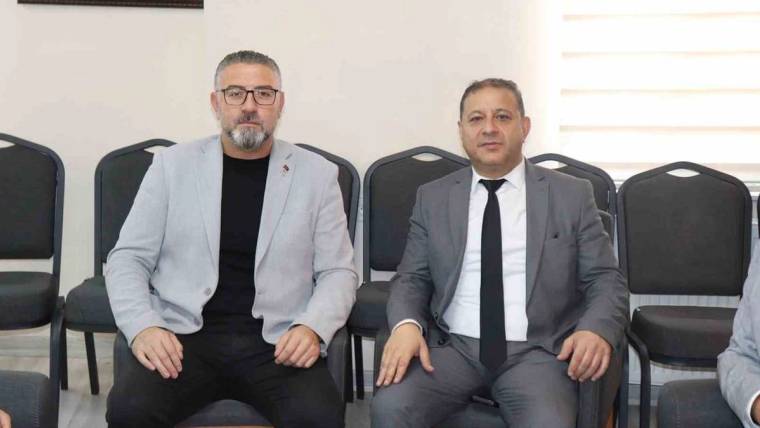 Toplantı salonunda yan yana oturan gözlüklü bir kişi ile takım elbiseli bir kişi, kameraya bakıyor.