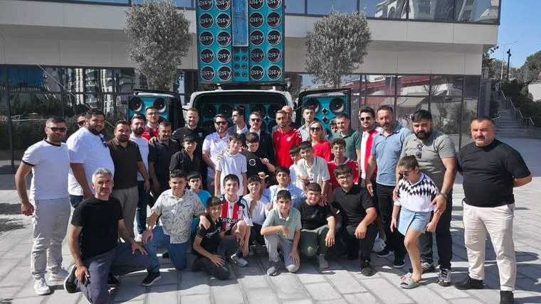 Bir bina önünde, aralarında kırmızı-beyaz formalar giyen çocukların da bulunduğu kalabalık grup poz veriyor.