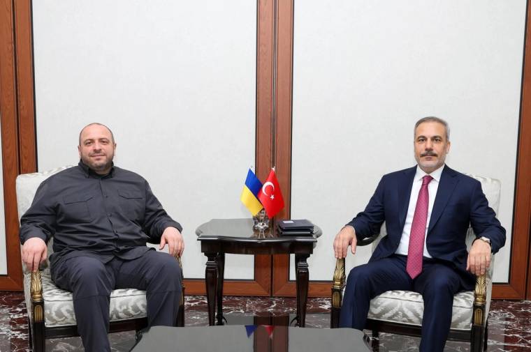 Bir odada iki kişi koltuklarda oturuyor; aralarındaki sehpanın üzerinde Türkiye ve Ukrayna bayrakları bulunuyor.