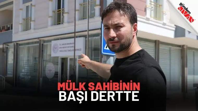 Bir kişi, önünde bulunan bir binaya işaret ediyor.